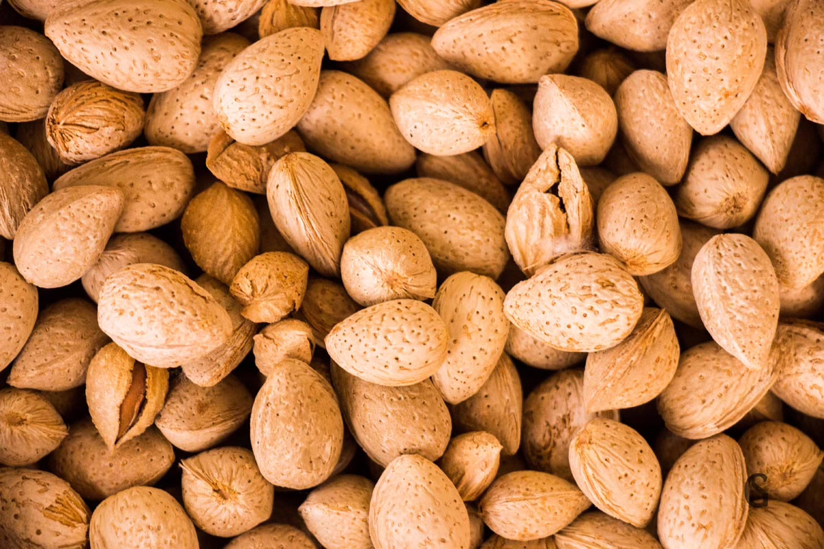 Pile of whole almonds in their shells. The almonds are a light brown color and have a textured surface.